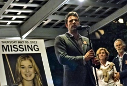 Ben Affleck davanti alla foto di Rosamund Pike con Lisa Banes e David Clennon sullo sfondo in una scena di L'amore bugiardo - Gone Girl