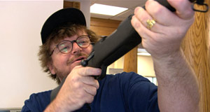 Il regista Michael Moore prova il fucile avuto in regalo da una banca per aver aperto un nuovo conto corrente